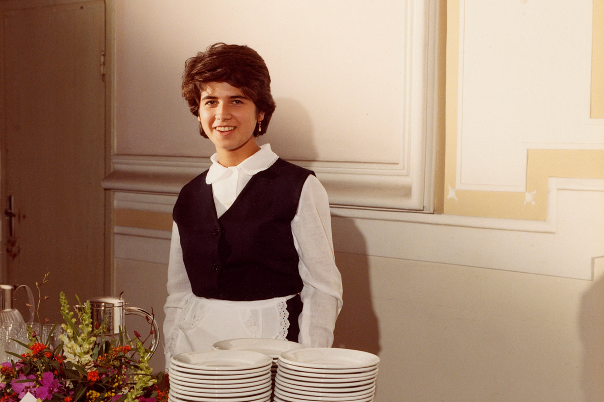 A young girl in a waitress dress smiling behind a set table